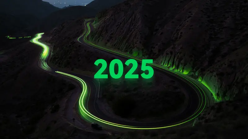 Green light trails trace a winding mountain road at night beneath large green 2025 numerals, marking t0ns year one